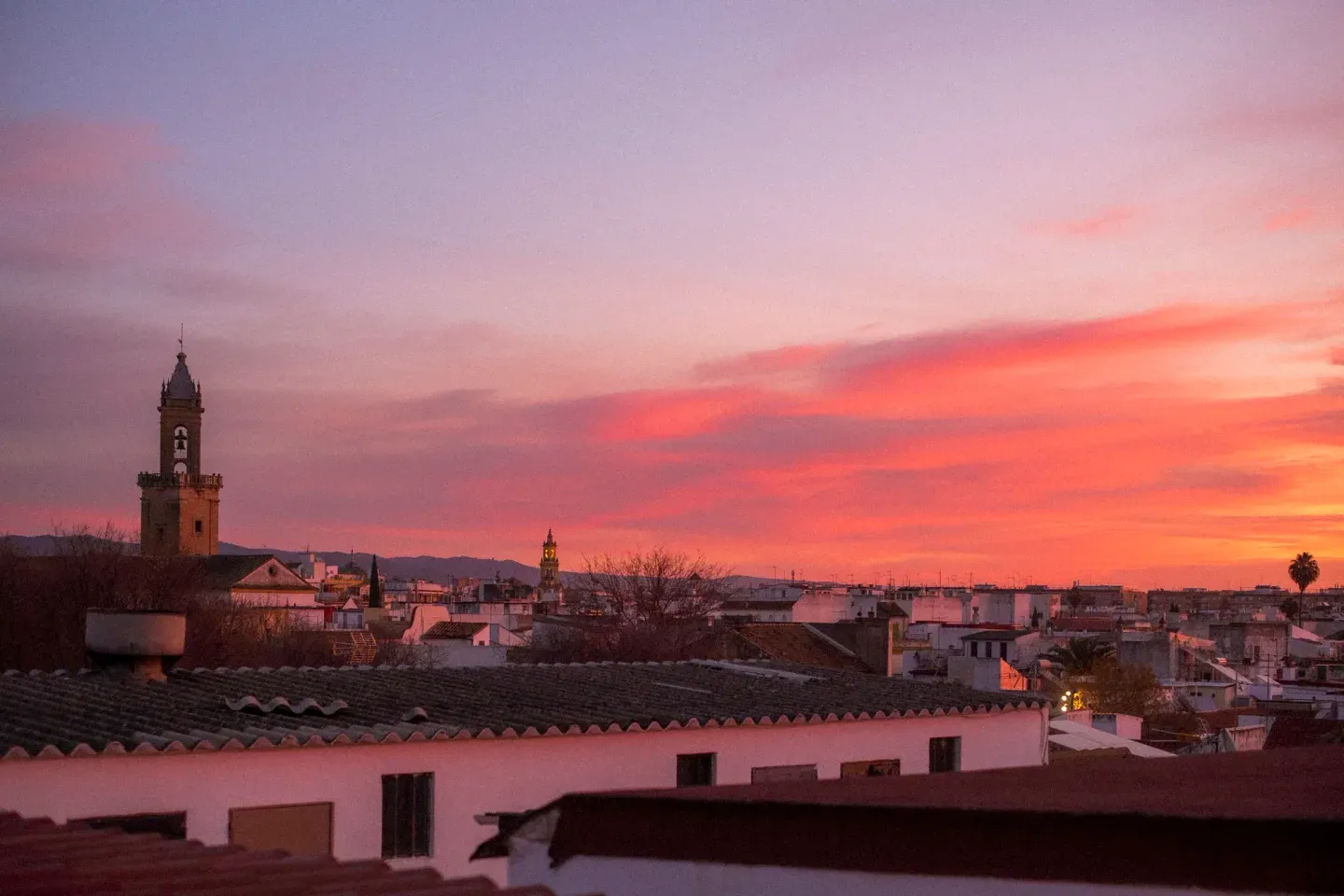 Sunrise over the rooftops of Cordoba, a bell tower against an orange and pink sky